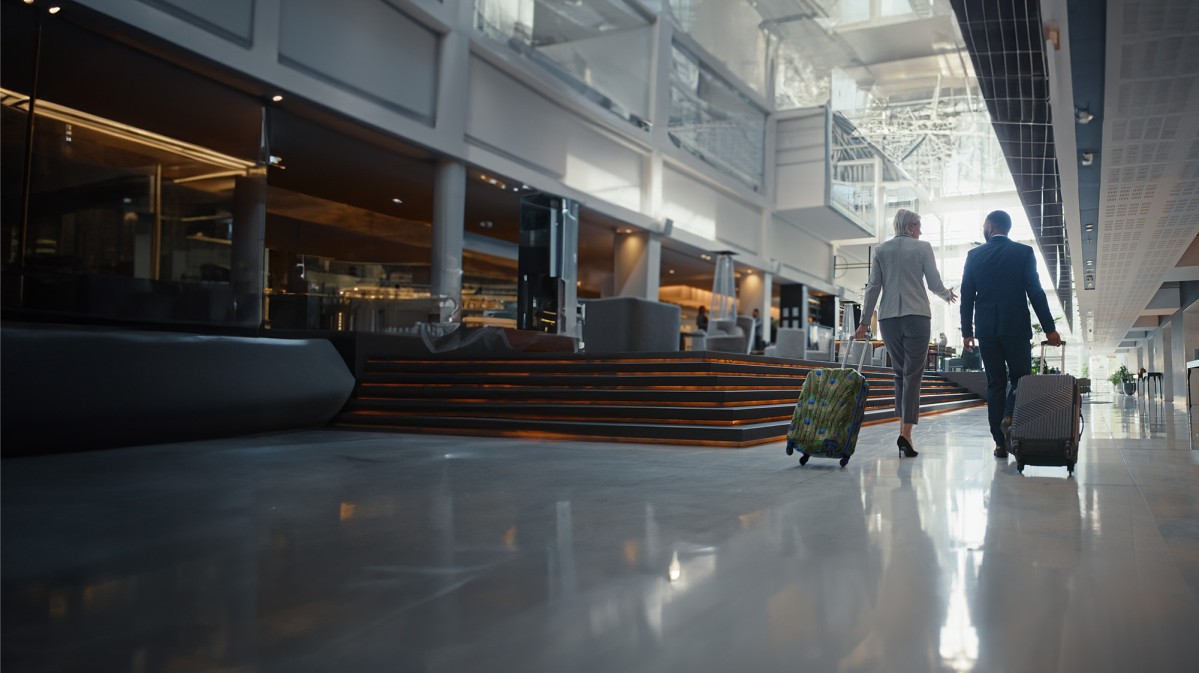 Two business professionals walking together through a hotel lobby, wheeling two small suitcases.