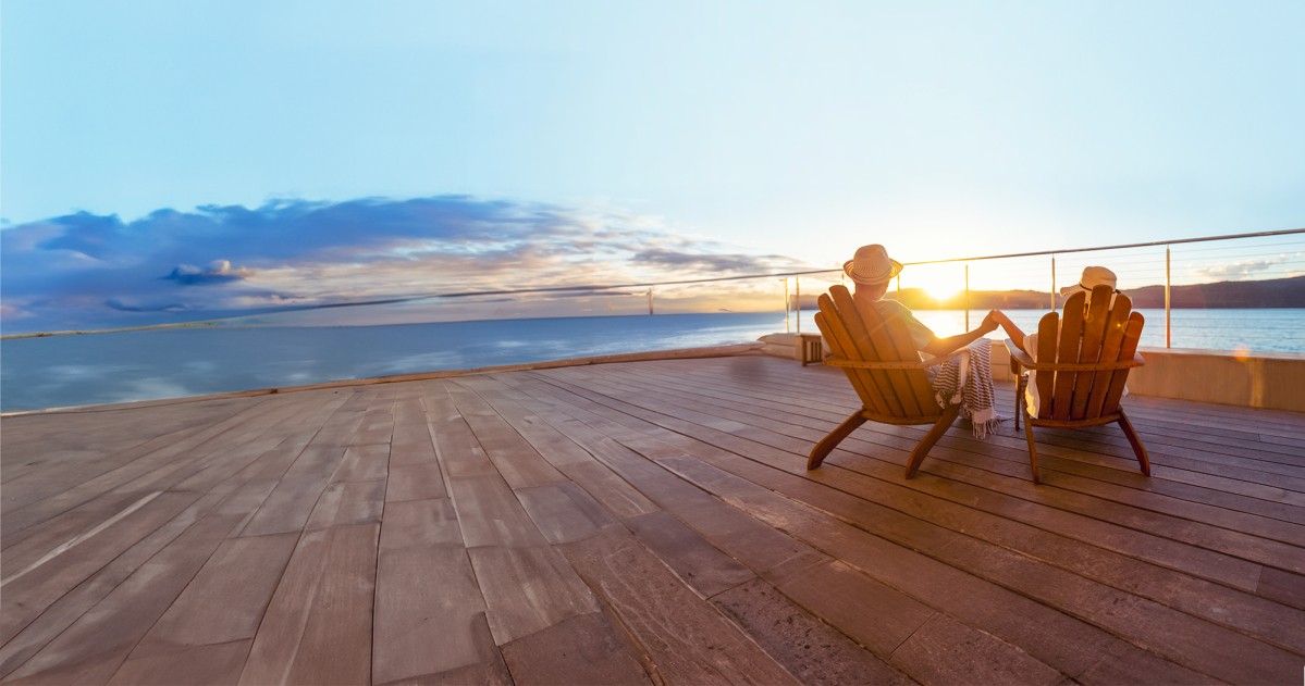 Couple holding hands and watching the sun set, sat in deckchairs on the deck of a boat